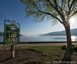 welcome to the village of lake george sign in front of the lake