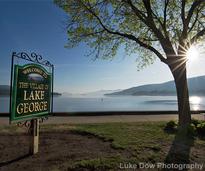 welcome to the village of lake george sign in front of the lake