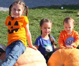 three kids sitting on pumpkins