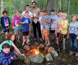 crew of campers and a counselor in woods at a campfire