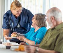 nurse serving a meal to two seniors at a nursing home