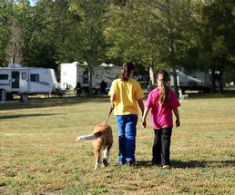 two girls walking through a campground with a dog on a leash