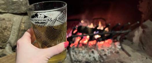 adirondack brewery beer glass held up in front of fire in fireplace