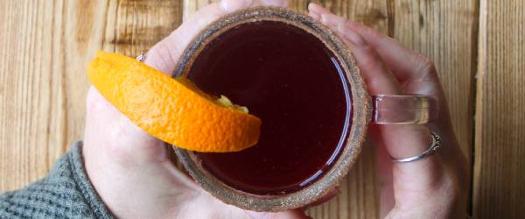 hands holding hot cocktail drink with lemon wedge