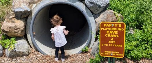 little girl looking into playground tunnel next to pappy's playground sign