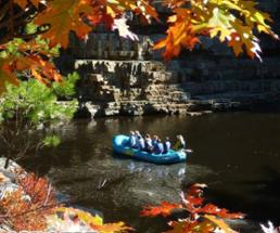 group on raft labeled ausable chasm drifting through chasm with fall leaves hanging overhead