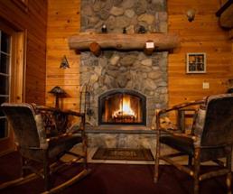 two chairs in front of a roaring fire in a cabin