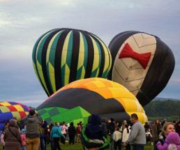 crowd at festival with three hot air balloons starting to lift off the ground