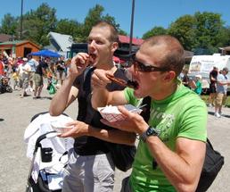 two guys eating barbecue food at a festival