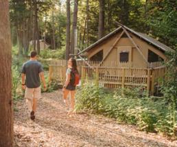 man and woman walking toward a glamping tent in the woods