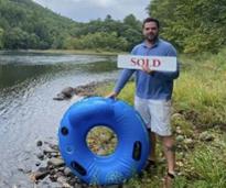 man with tube and sold sign stands by river