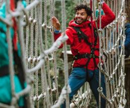 man traversing a rope net in the treetops