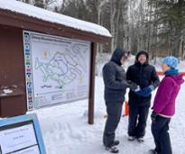 three people at a hiking trailhead in the winter