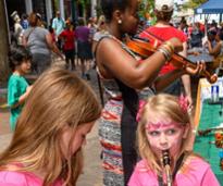 two kids, one with an instrument, and woman with violin at festival