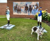 dog poses in front of lawn jockeys and horse racing mural 