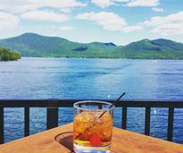 drink in a rocks glass on a table with lake george in the background