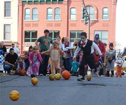 kids dressed in halloween costumes playing pumpkin bowling on a street
