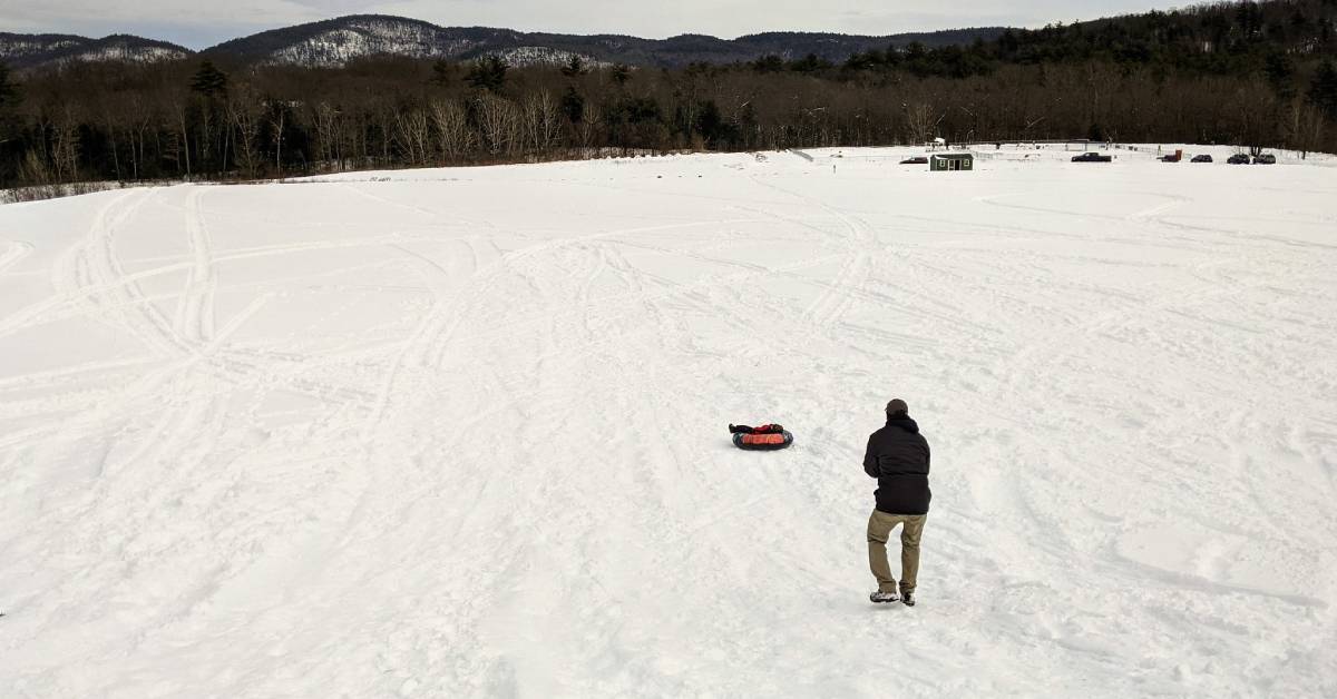 man standing near kid sliding down a hill in a snow tube