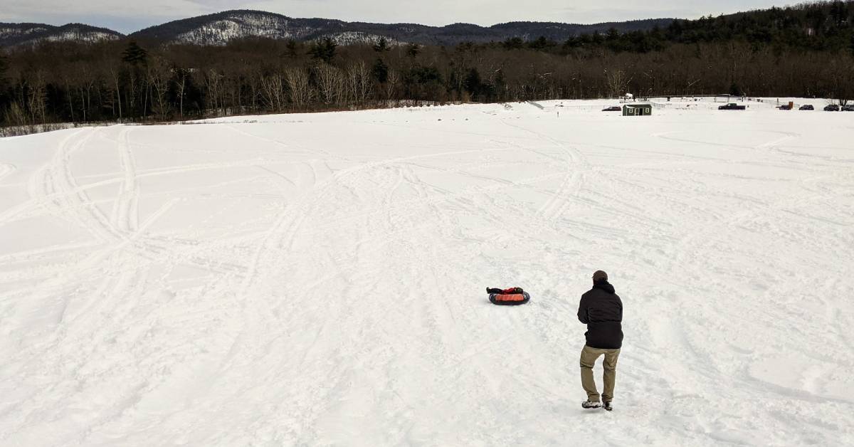 a man watching as a child rides down a snowy hill in a snow tube