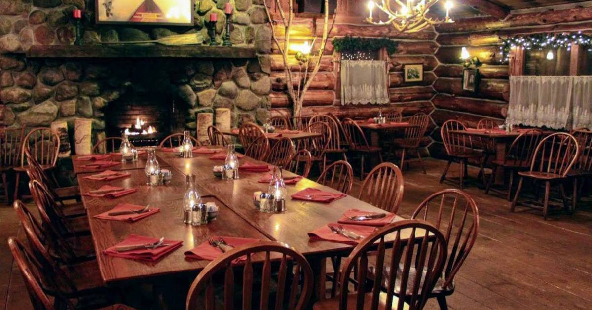 restaurant dining room with tables, wooden walls, and a large stone fireplace