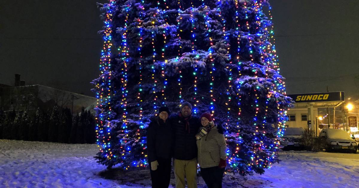 three people posing in front of giant lit tree