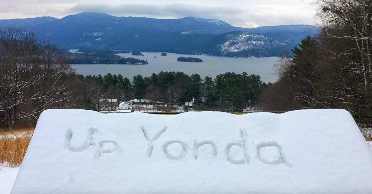 view of a lake and mountains and a roof with the words up yonda written in snow on top
