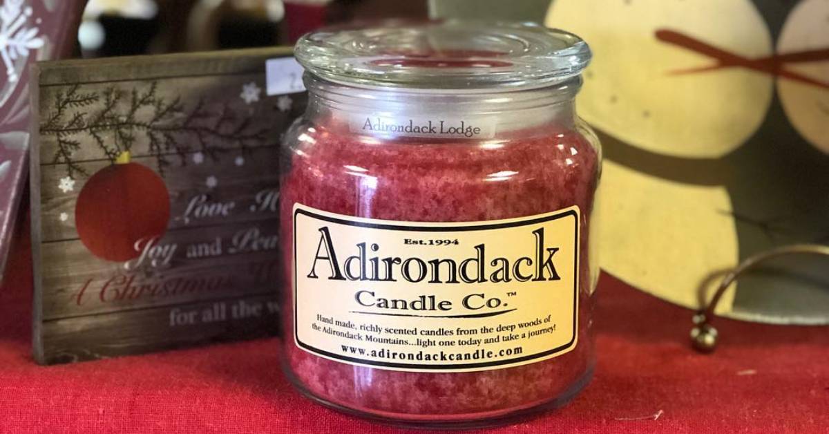a red glass candle with an adirondack candle co logo