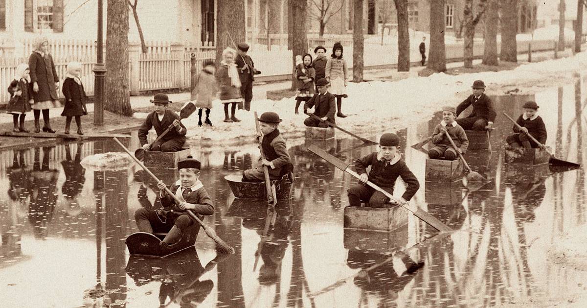black and white photo of kids in cardboard boats in a flood