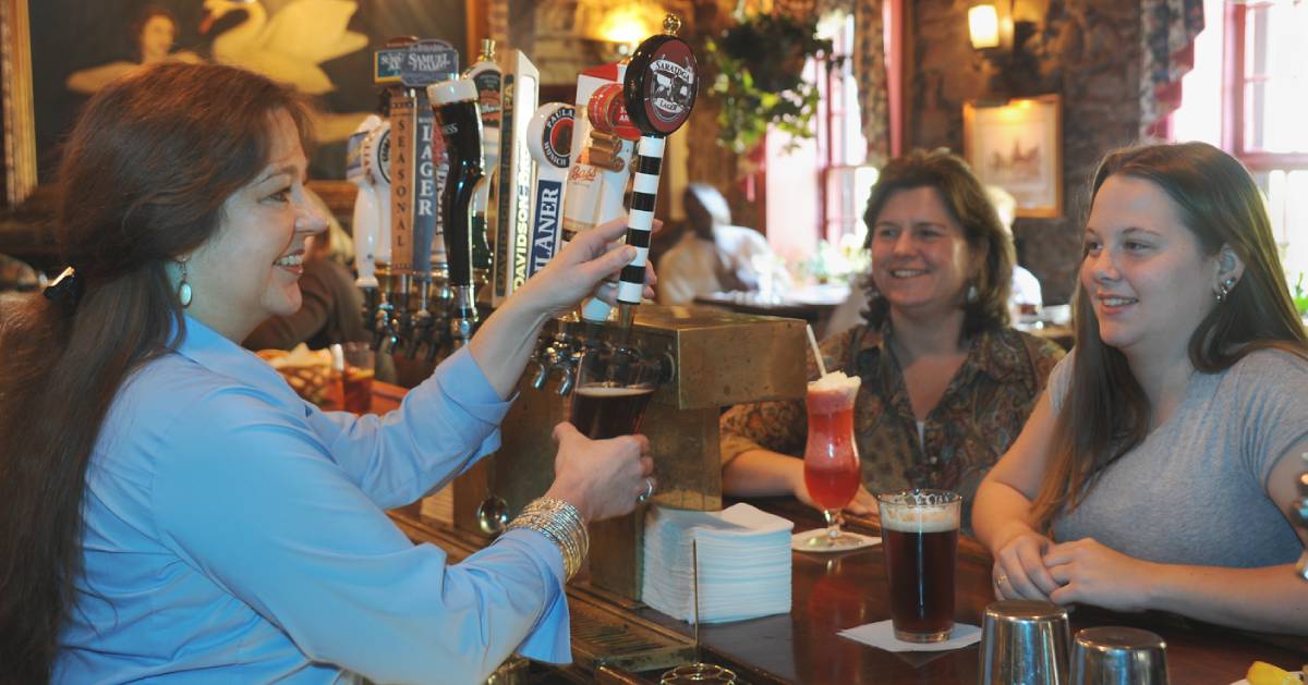 two women at a bar, with a female bartender pouring beer into a glass