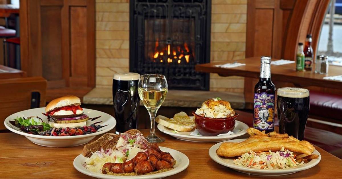 plates of food and drinks on a table with a fireplace in the back of the restaurant