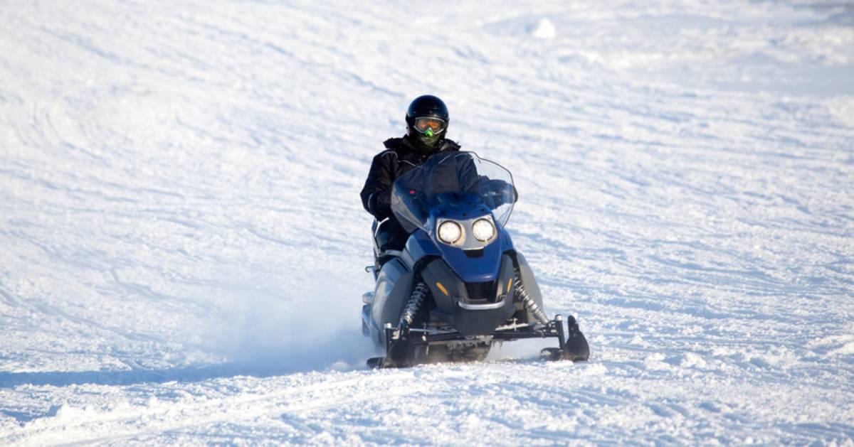 snowmobiler riding across snowy ground