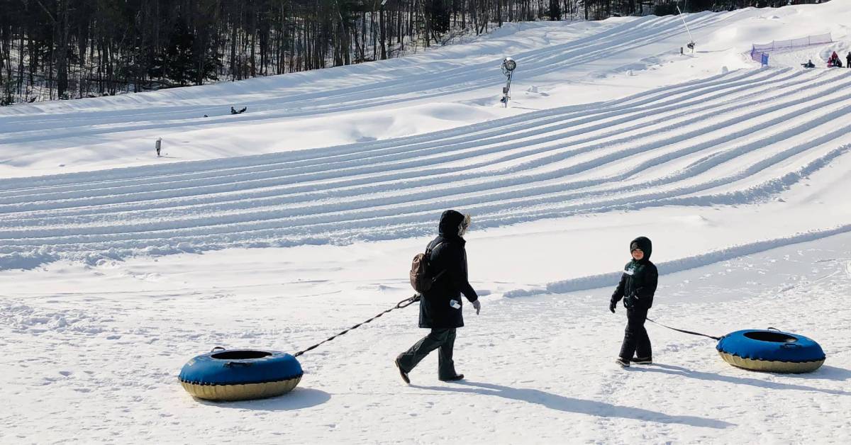 an adult and a kid with snow tubes at a snow tube park