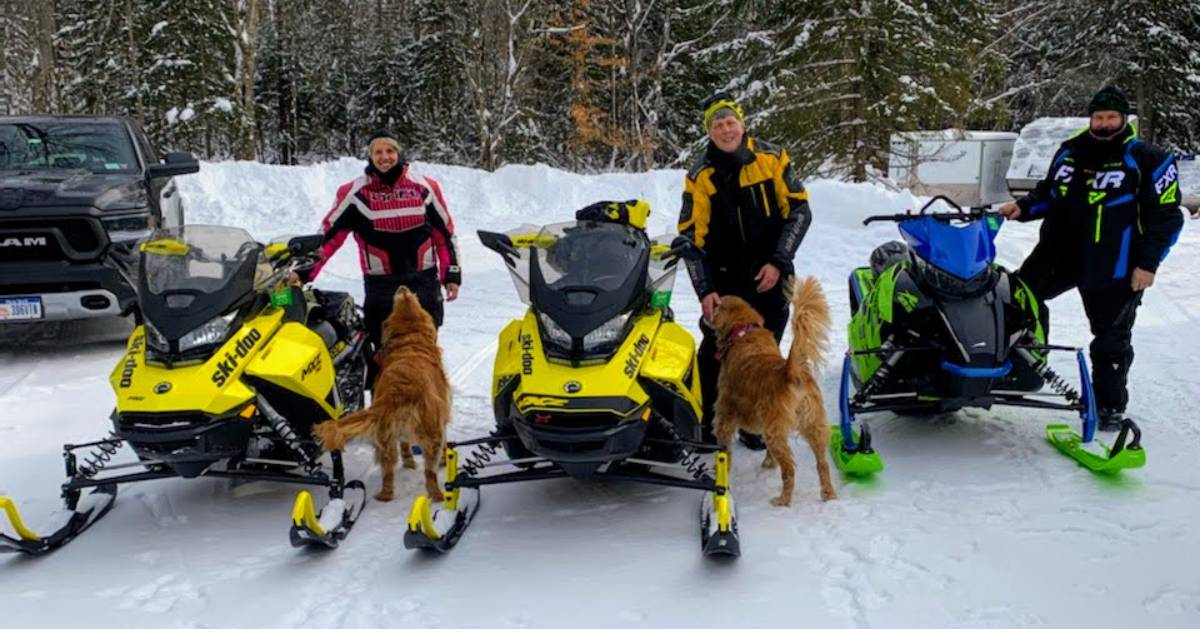 three men with their snowmobiles, two dogs