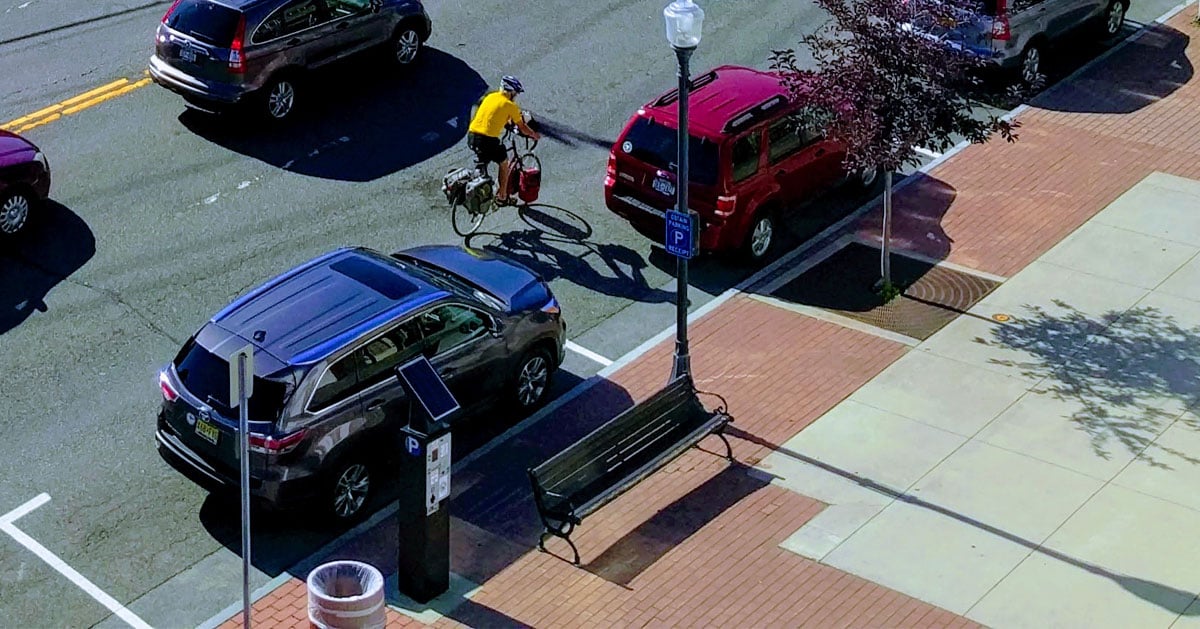 man rides bike next to parked cars