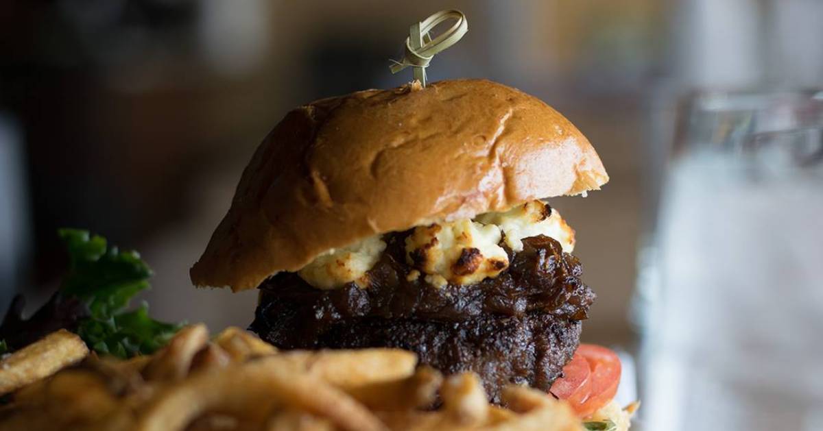 a burger with goat cheese, fries and a glass of water in the foreground