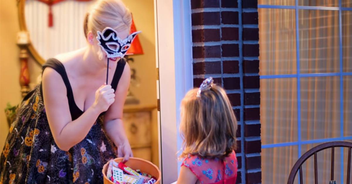 a woman with a masquerade ball mask answering the door for a little girl trick-or-treating