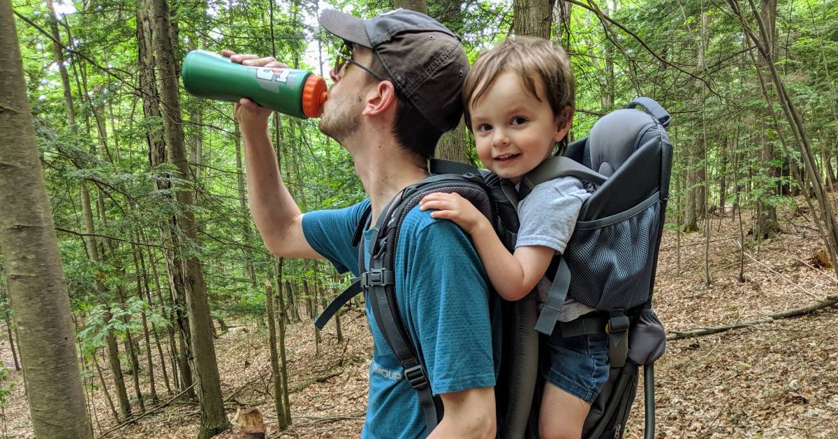 hiker with kid on back drinks water