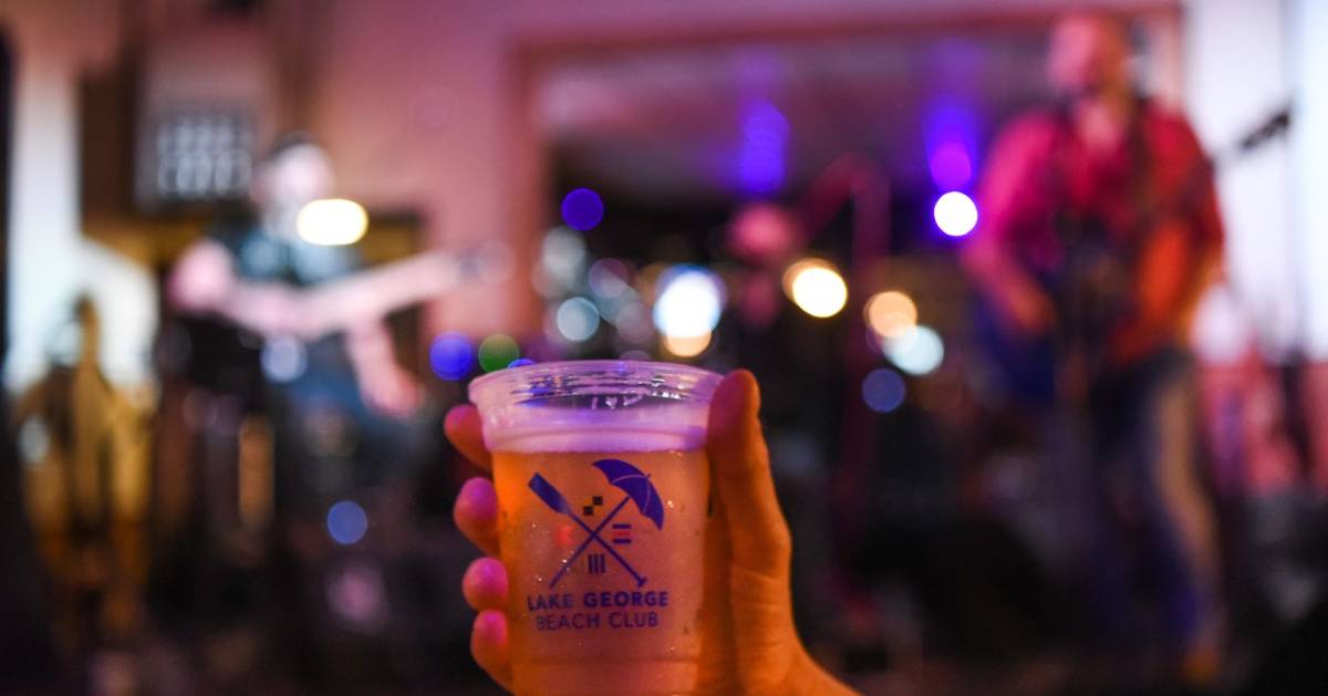 beer held up with backdrop of band playing