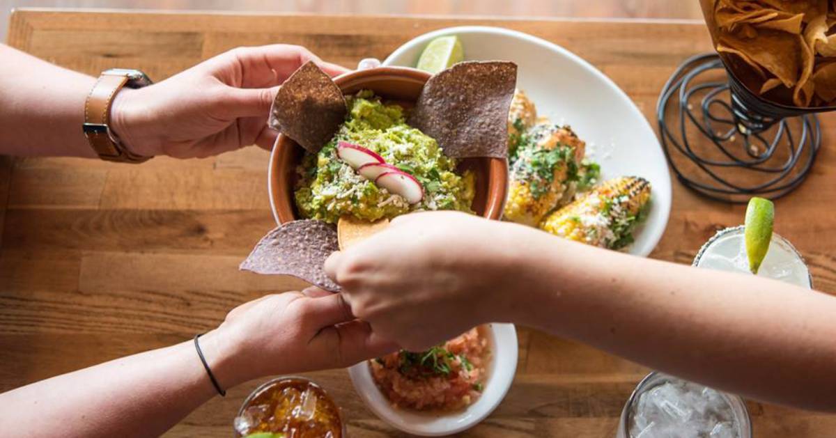 hands reaching for chips dipping in guacamole