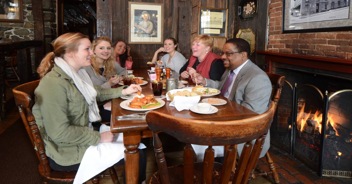 group of people eating at a table by a fireplace