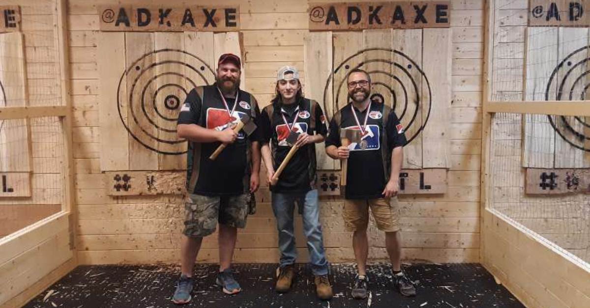 three men smiling and standing in front of axe targets holding axes