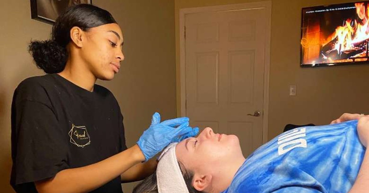 a woman with blue gloves on applying skincare product to the face of a woman laying down 