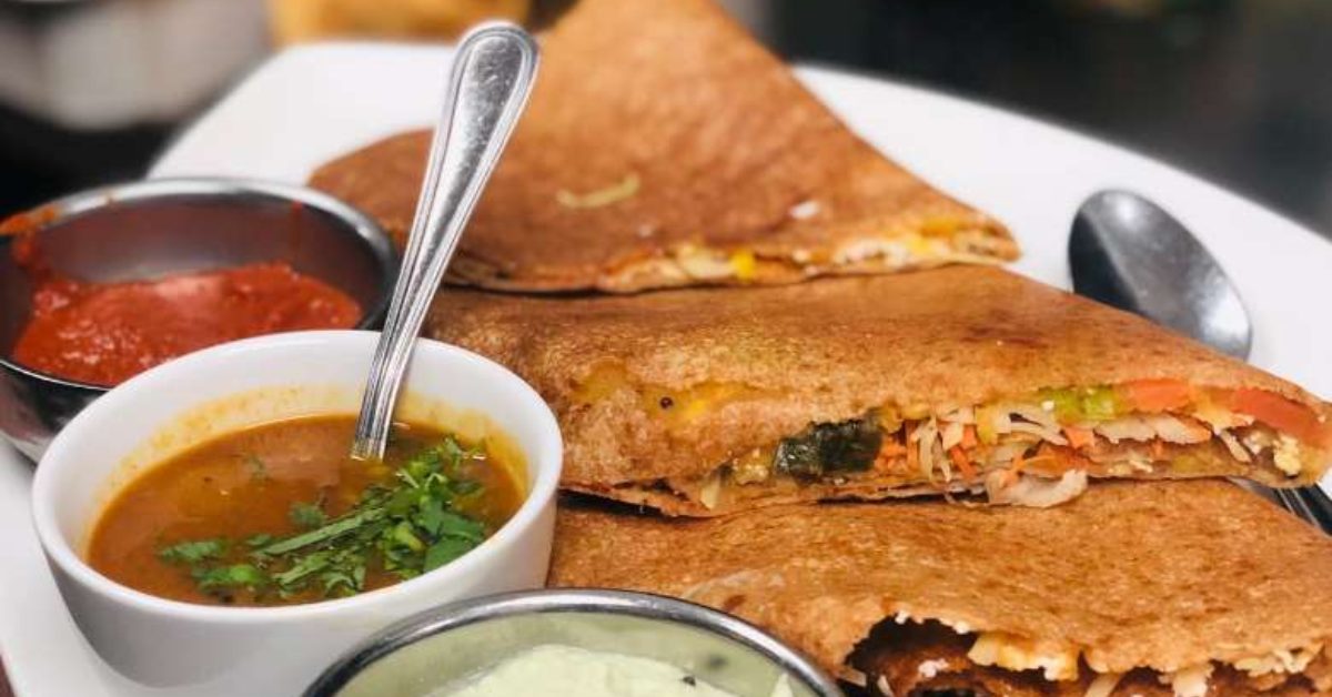 Indian crepes with multi-color veggie filling next to three sauces, all on a white plate