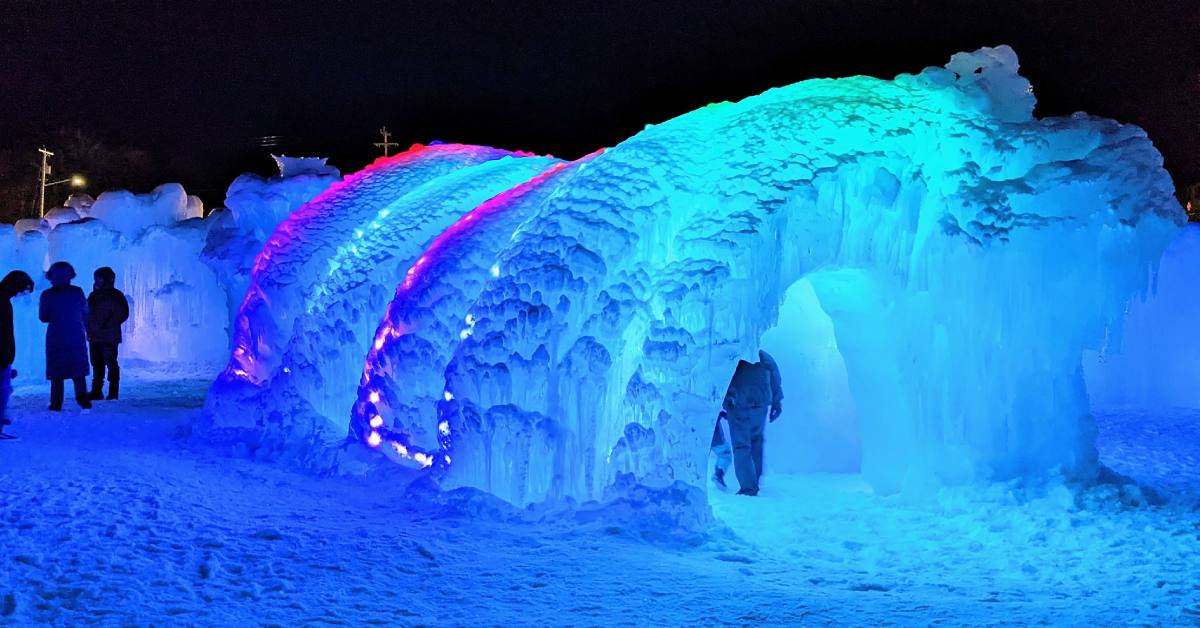 people walking around ice castles lit up at night