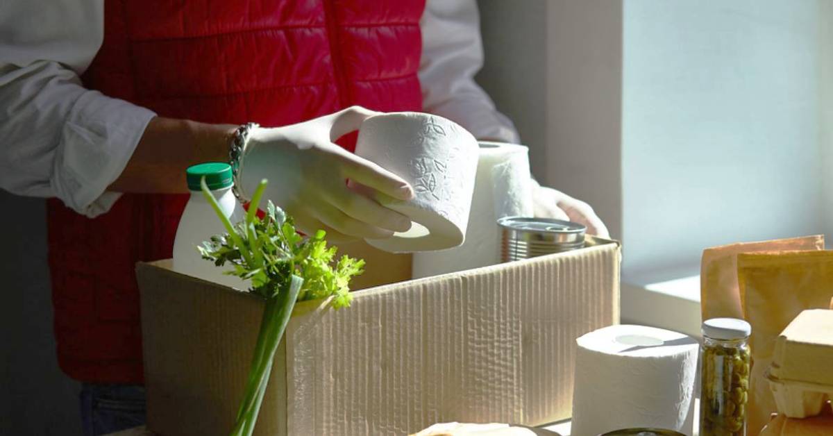 man wearing gloves putting food and toiletries into a box