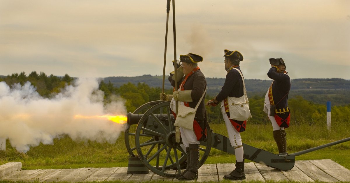 men dressed for reenactment by a cannon that is firing