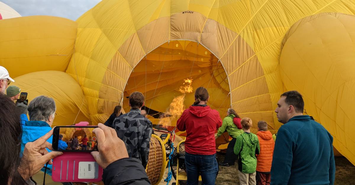 people watching and taking photos of fire going into hot air balloon