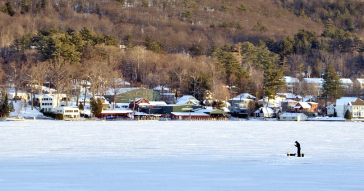 one person ice fishing with view of town and mountains in the background