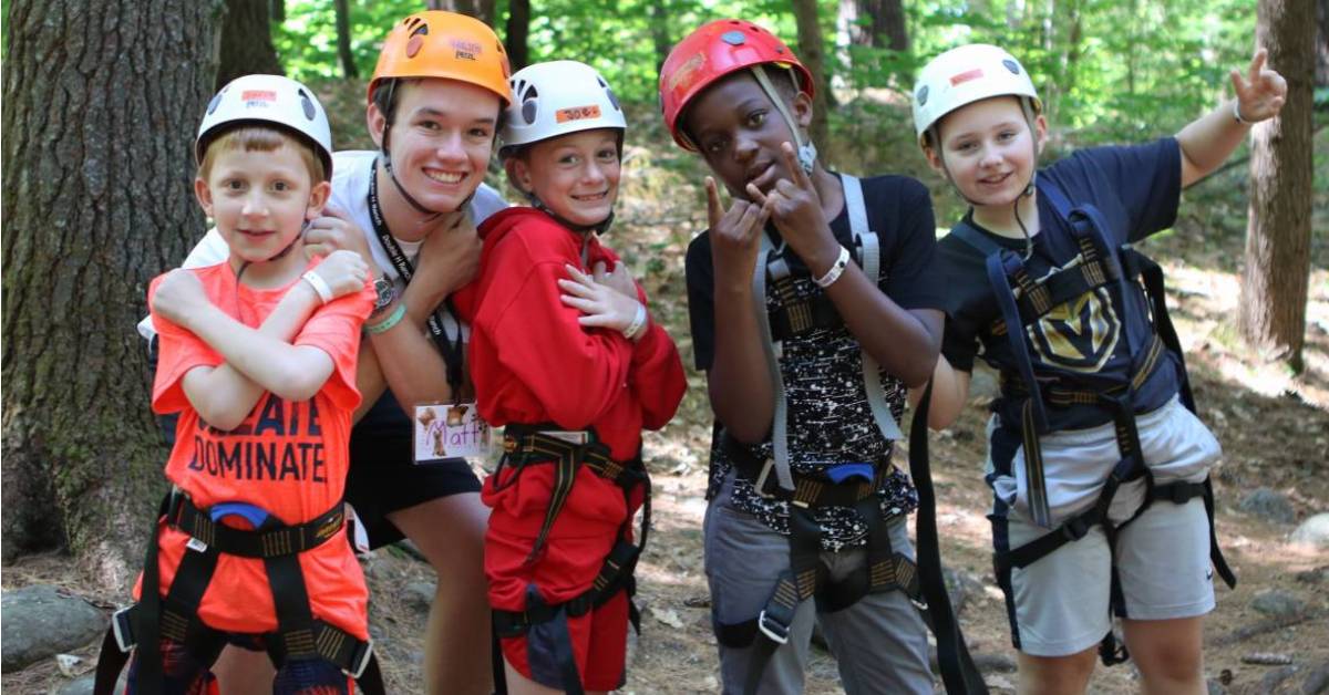 four boys and a young adult man wearing helmets outdoors near trees