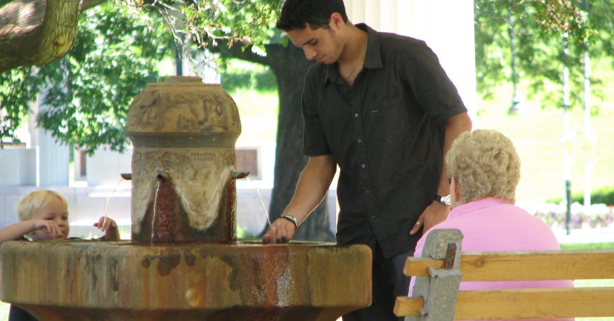 man, woman, and child near a mineral spring fountain